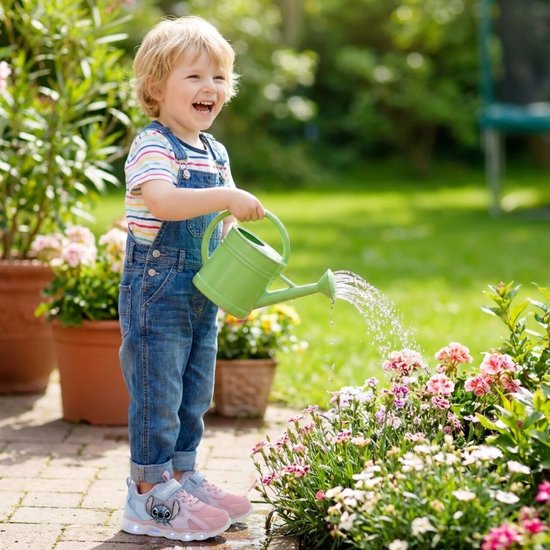 Jongetje met tuinwaterpomp, draagt spijkerbroek met tuinbroek en gestreepte t-shirt, met lichtgevende roze sneakers.