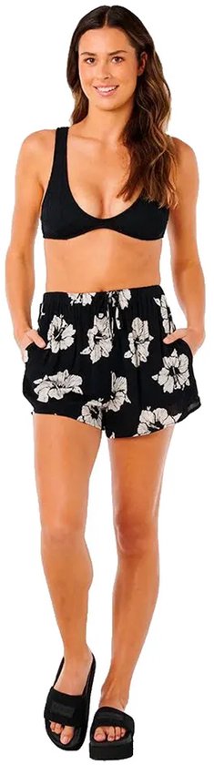 Model draagt korte zwarte broek met witte bloemenprint en zwart bikinibovenstuk.