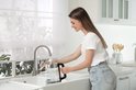 Vrouw vult een glazen waterkoker onder de kraan in een keuken.