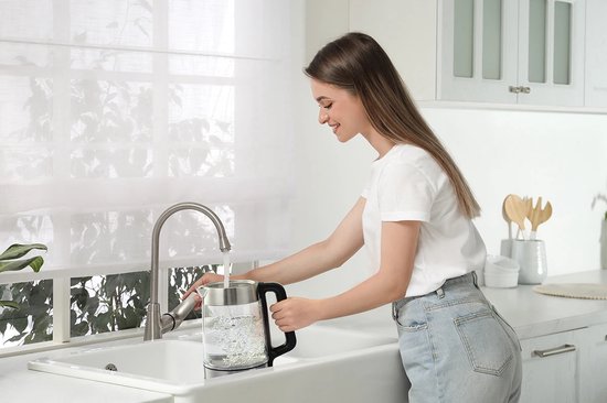 Vrouw vult een glazen waterkoker onder de kraan in een keuken.