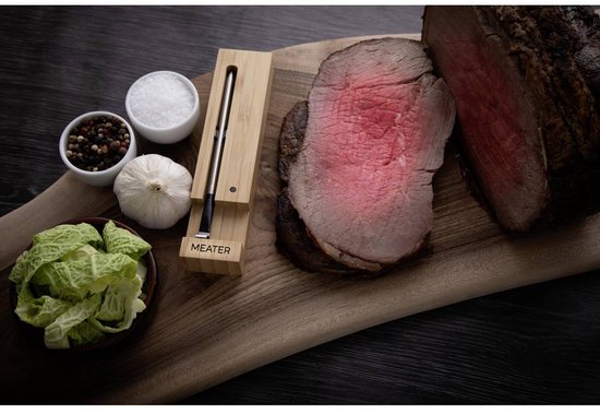 Geroosterd rosbief op een houten plank, met knoflook, zout en peper, en een Meater thermometer.