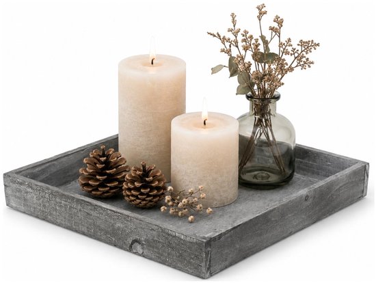 Gedecoreerd grijs houten dienblad met twee witte stompkaarsen, dennenappels en gedroogde bloemen in een vaasje.