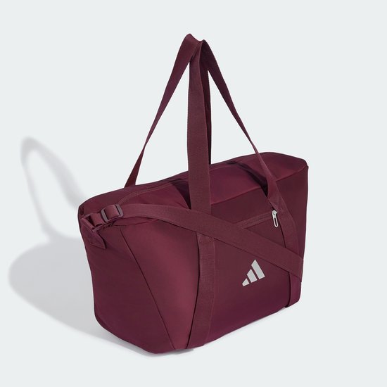 Bordeauxrode sporttas met hengsels, een schouderband en een zilverkleurig Adidas logo, schuin van voren gefotografeerd.