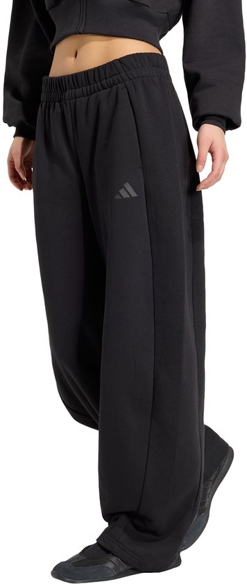 Model dat een zwarte wijde broek met Adidas logo draagt.