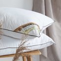Twee witte kapok kussens met bruine bies, op een houten bankje.