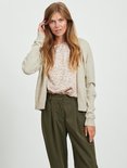 Model draagt een beige gebreid vest over een bloemenprint top en olijfgroene broek.