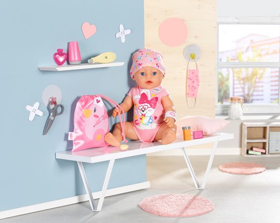 Baby pop zittend op een bankje met doktersthermometer, roze tas, masker en kleding.