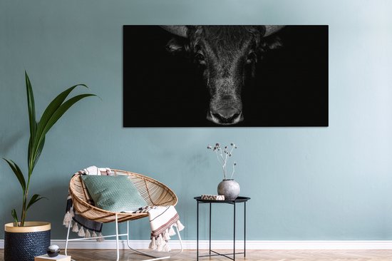 Toile noir et blanc d'un taureau sur fond sombre, au-dessus d'une chaise et d'une table d'appoint.