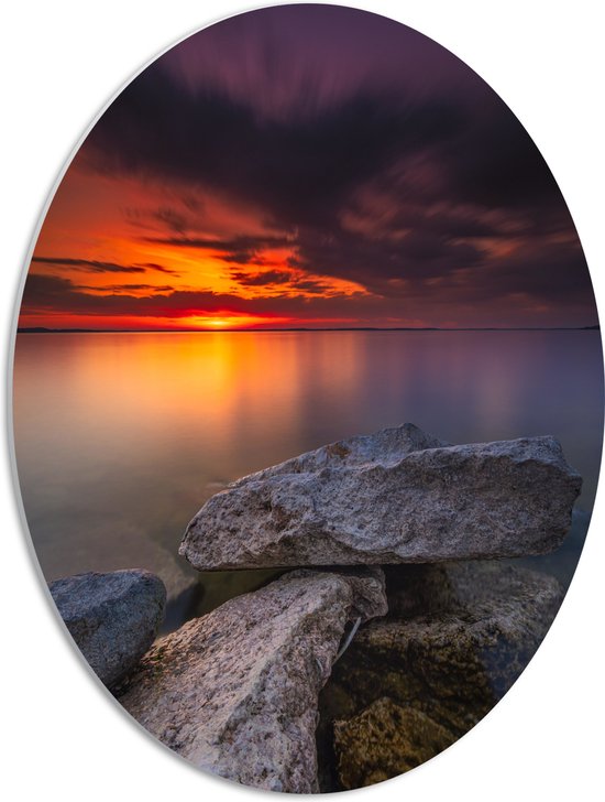 WallClassics - PVC Schuimplaat Ovaal - Kleine Rotsen aan het Water met Zonsondergang - 42x56 cm Foto op Ovaal  (Met Ophangsysteem)