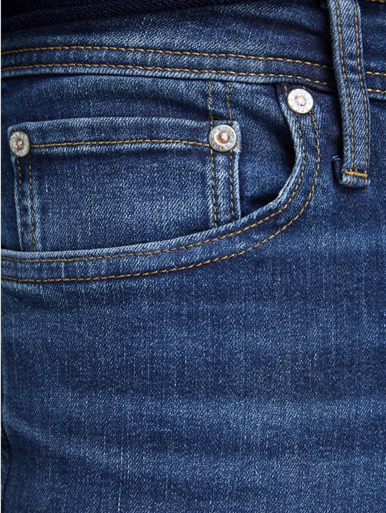 Detail van de voorkant van een donkerblauwe spijkerbroek met een klein zakje, bruine stiksels en knopen.