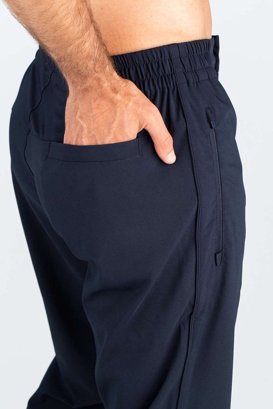 Donkerblauwe sportbroek met elastische tailleband, een hand in de zak en een ritszak op de zijkant.