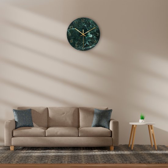 Groene marmerlook wandklok met gouden wijzers, opgehangen boven een beige bank.