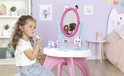 Meisje met krullend haar zit op een krukje en gebruikt make-up aan de Gabby's Dollhouse kaptafel.
