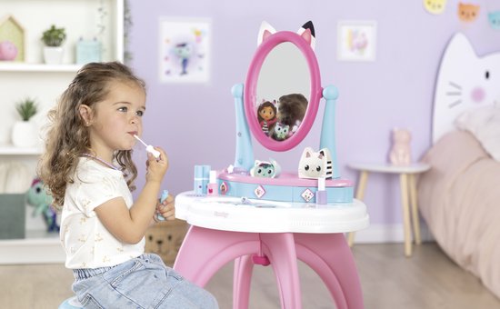 Meisje met krullend haar zit op een krukje en gebruikt make-up aan de Gabby's Dollhouse kaptafel.