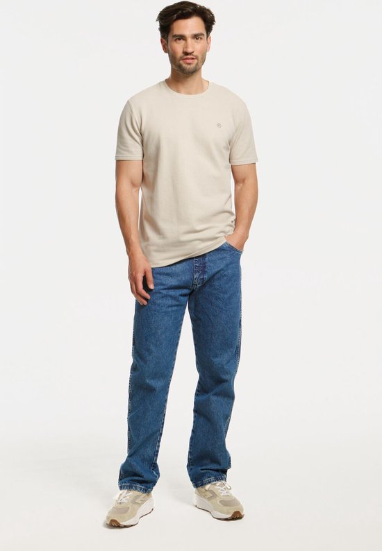 Man in een beige shirt en rechte blauwe jeans.
