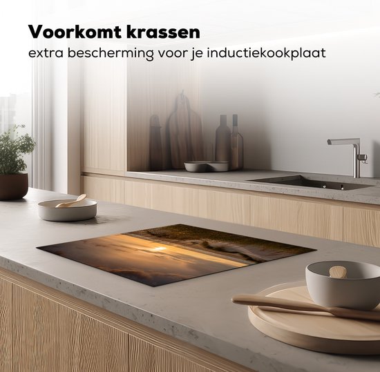 Inductiebeschermer met duinenlandschap bij zonsondergang op een aanrecht in een moderne keuken.