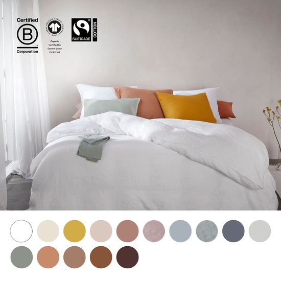 Bed opgemaakt met wit linnen, met diverse decoratieve kussens in zachte kleuren.