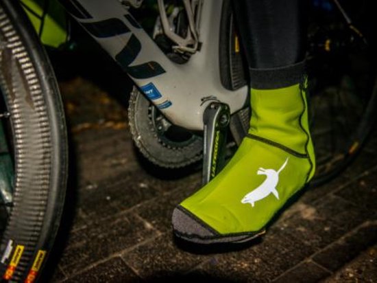 Een fietser draagt een neongele Sealskinz overschoen met grijze zeehond.