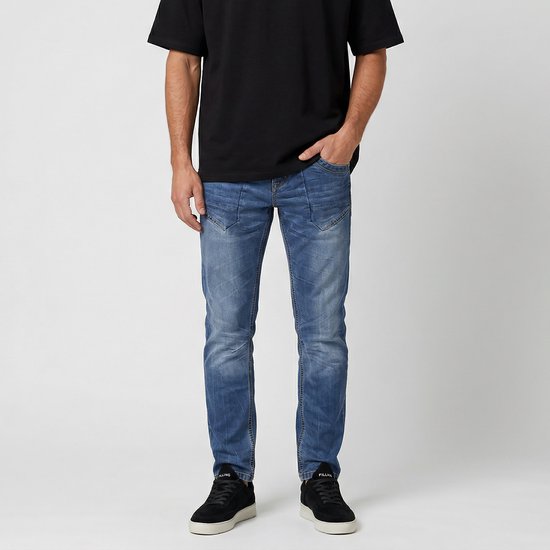 Blauwe jeans met subtiele plooien bij de zakken en een stone wash. Gedragen door een man met zwarte sneakers en een zwart T-shirt.