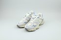 Twee New Balance sneakers in beige en lichtblauw, met witte veters, op een grijze achtergrond.