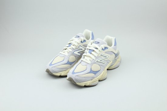 Twee New Balance sneakers in beige en lichtblauw, met witte veters, op een grijze achtergrond.
