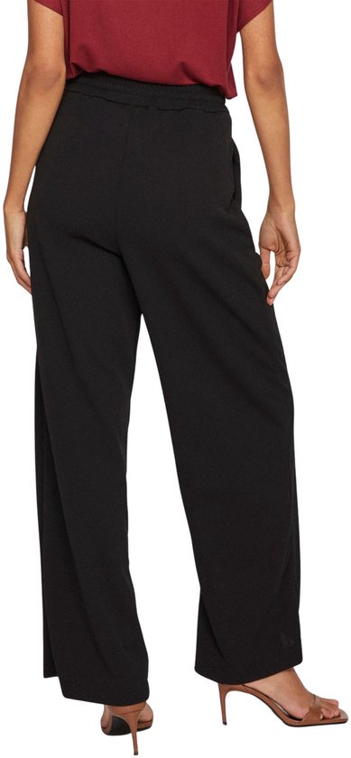 Model van achteren gezien, draagt een zwarte wijde broek en bordeauxrode top.