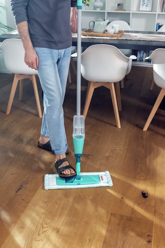 Man met Leifheit Easy Spray XL vloerwisser op een houten vloer bij een eettafel.
