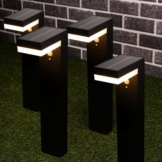 Vier zwarte staande tuinlampen met zonnepaneel en bewegingssensor, witte ledverlichting aan de bovenzijde, op gras.