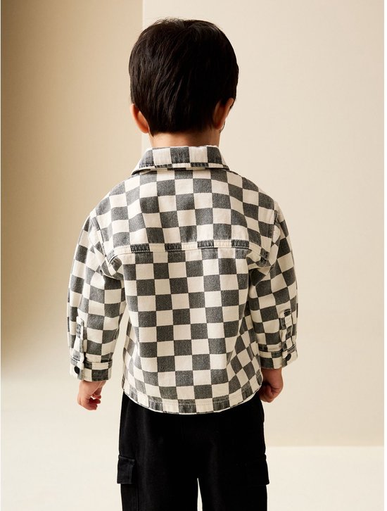 Achterkant van een jongen in een grijs-wit geblokt overshirt, zwarte broek en sneakers.