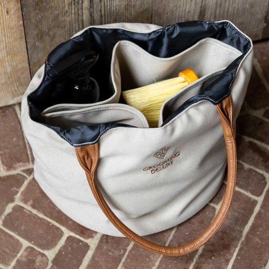 Open beige canvas tas met bruine leren hengsels, gevuld met poetsspullen. Zwarte binnenzijde met vakken.
