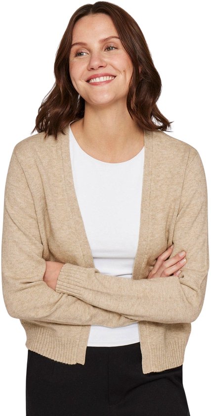 Model draagt een beige gebreide vest open aan de voorkant, met lange mouwen en een witte top eronder.