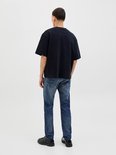Man in een zwarte oversized T-shirt en blauwe jeans, met de rug naar de camera.