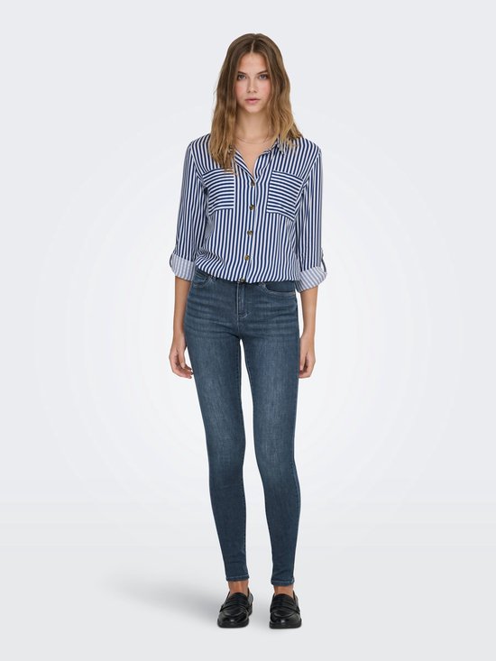 Model in een gestreepte blouse en donkerblauwe skinny jeans, gezien van voren. Gestreepte blouse met opgerolde mouwen en zwarte loafers.