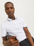 Man zit en draagt een wit poloshirt met zwarte bies op kraag en mouwen.