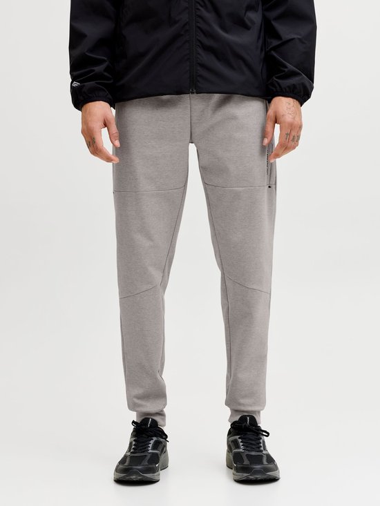 Grijze joggingbroek met strakke broekspijpen en 'JJ Athletic Dept.' opdruk, gedragen met zwarte sneakers.