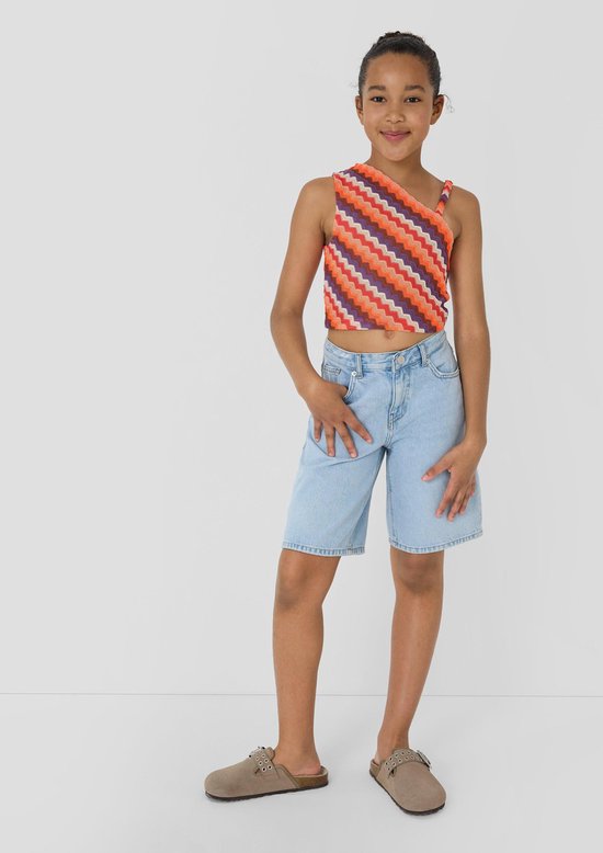 Meisje met een gekleurde top met zigzagprint en een lichtblauwe denim bermudashort.