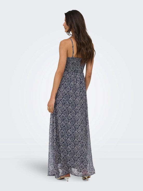 Maxi jurk met spaghettibandjes in marineblauw met een witte geometrische print, gedragen door een vrouw die met haar rug naar de camera staat.