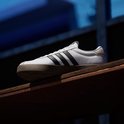Witte Adidas VL Court 3.0 sneaker met zwarte strepen en bruine zool, tentoongesteld op een houten plank.