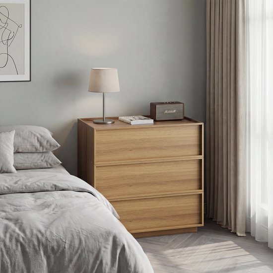 Ladekast met 3 laden in eikenlook, naast een bed, met een lamp en radio erop.