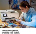 Jonge vrouw met blauwe hoodie gebruikt haar smartphone terwijl een witte HP printer op tafel staat, omringd door foto's.