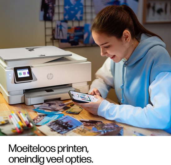 Jonge vrouw met blauwe hoodie gebruikt haar smartphone terwijl een witte HP printer op tafel staat, omringd door foto's.