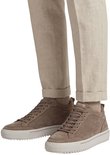 Benen van een man met beige broek en taupe Rehab sneakers met crèmekleurige zolen.
