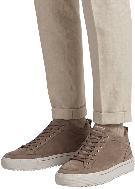 Benen van een man met beige broek en taupe Rehab sneakers met crèmekleurige zolen.