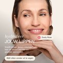 Model met een lichte glimlach, handen bij de kin. Tekst: 'hydrateer JOUW LIPPEN'. Kleur "Dusty Rose".
