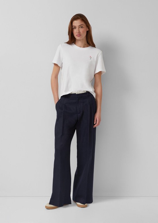 Model in donkerblauwe wijde broek met gestreepte tailleband en wit T-shirt met kleine bloem.