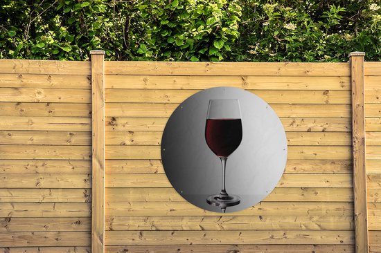 Rond tuinposter met glas rode wijn op grijs witte achtergrond, hangend aan houten schutting.