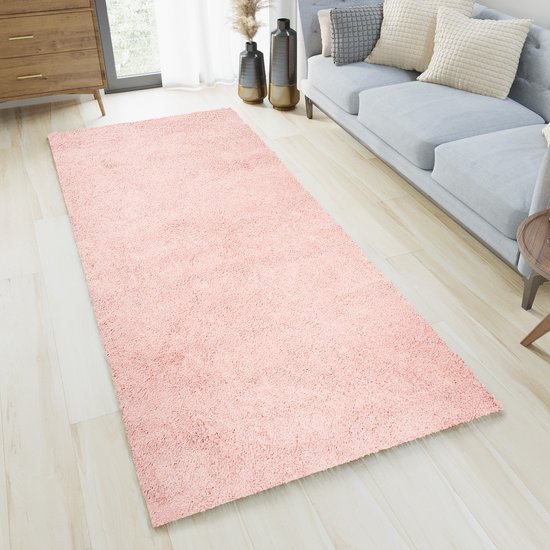 Un tapis rose pâle à poils longs dans un salon, à côté d'un canapé gris.