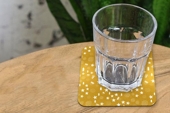 Sous-verre doré à motif de Noël blanc sous un verre d'eau sur une table en bois.