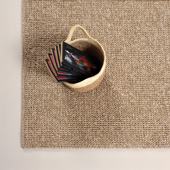 Un tapis brun à l'aspect jute, avec un panier de livres posé dessus.