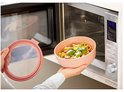 Een persoon haalt een roze kom met pasta en groenten uit een magnetron.